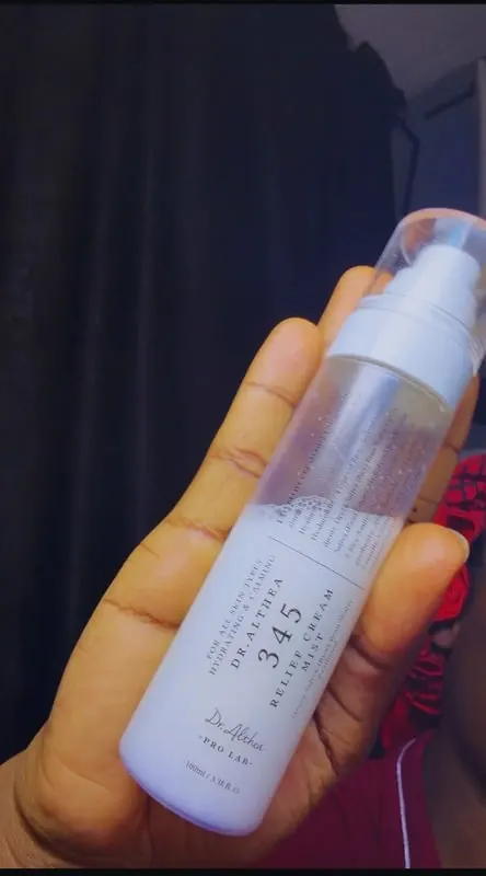 Hand holding a face mist bottle against a dark backdrop